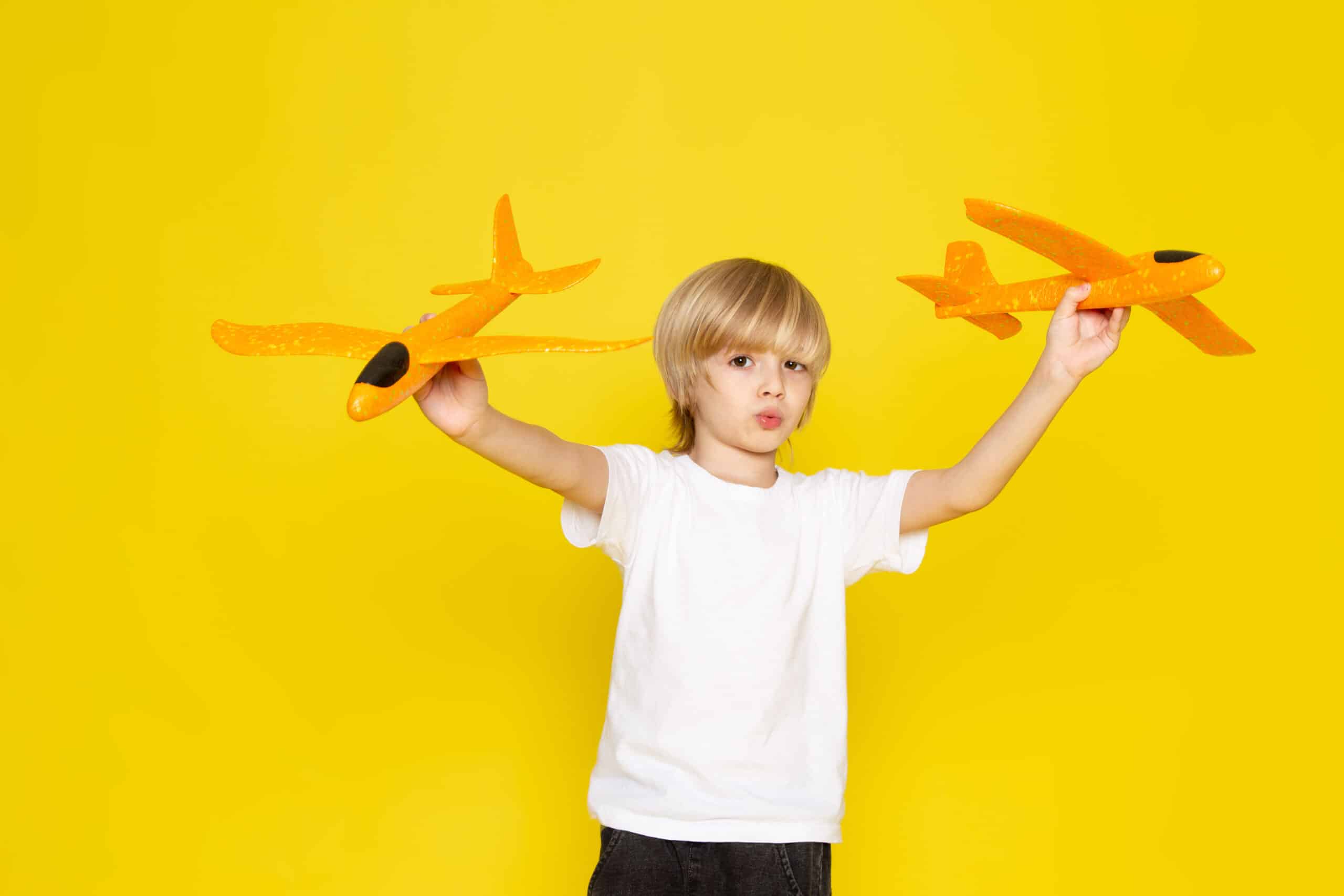 Child holding toy airplanes against a yellow background