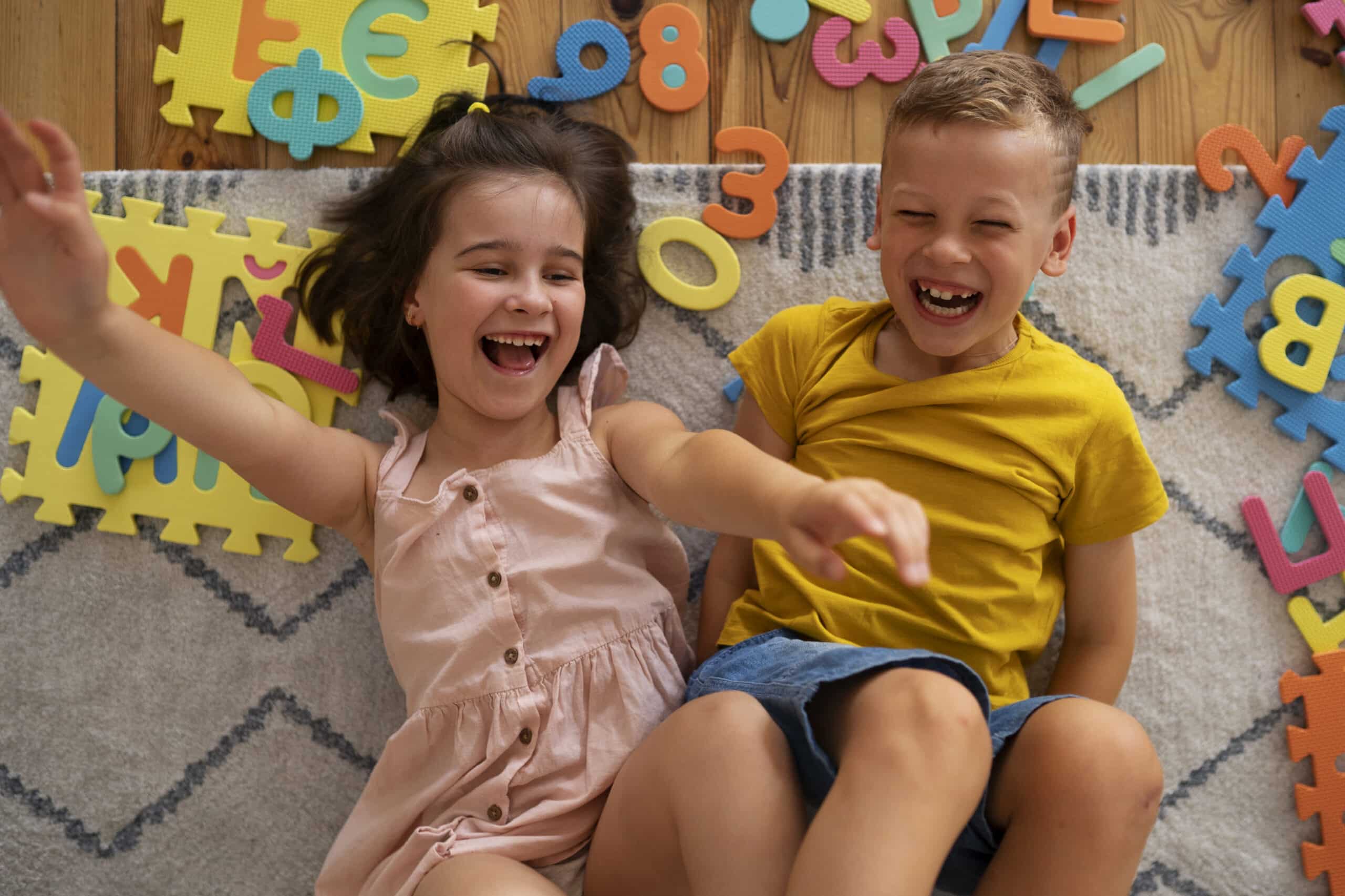 Young boy and girl laughing while sitting on floor with colorful alphabet foam puzzle pieces